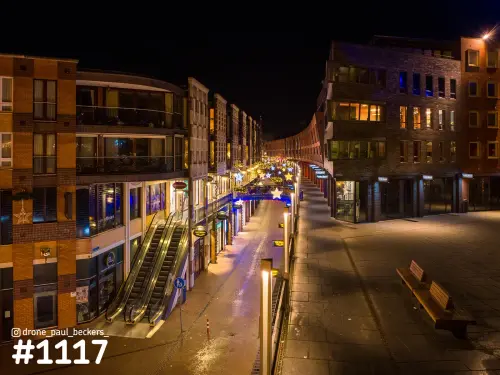 Nijmegen van boven in de avond: natte winkelstraat met roltrappen, bakstenen gevels en verlichte sterren boven de straat
