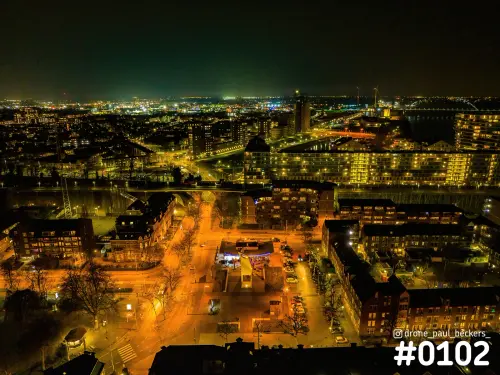 Luchtfoto van een woonwijk in Nijmegen bij avond, met oranje straatverlichting en een verlicht appartementencomplex