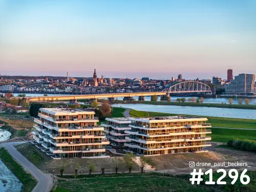 Luchtfoto van de Nimbus-appartementen in Nijmegen-Lent aan de Nevengeul, met Stevenskerk en brug in gouden licht
