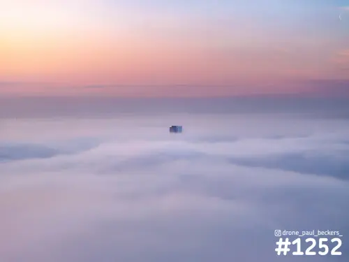Luchtfoto van de top van Nimbus in Nijmegen die boven een dik mistdek uitsteekt, onder een roze en paarse lucht