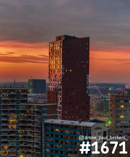 Woontoren Nimbus in Nijmegen met donkerrode gevel in avondlicht, oranje lucht en verlichte ramen boven de flats
