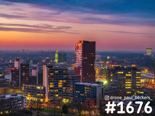 Luchtfoto van Nimbus en flats bij het Stationsgebied in Nijmegen in de schemering, met verlichte ramen en een roze lucht