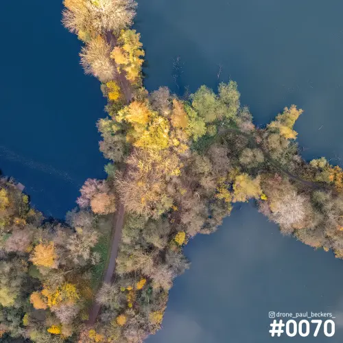 Luchtfoto recht van boven op een smalle landtong met herfstbomen en een pad tussen donkerblauw water in de Ooijpolder