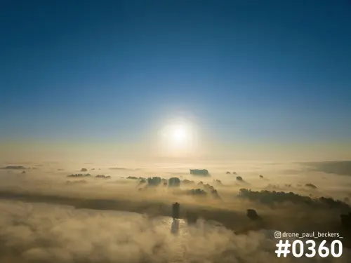 Luchtfoto van de Ooijpolder bij zonsopkomst, met dikke mist boven de rivier en boomgroepen die uit het wolkendek steken