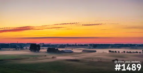 Luchtfoto van de Ooijpolder bij Nijmegen bij zonsopkomst, met laaghangende mist over weilanden en boerderijen onder een oranje lucht
