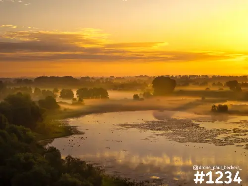 Luchtfoto van de Ooijpolder bij zonsopkomst, met mist boven een kronkelende plas en bomen in oranje licht