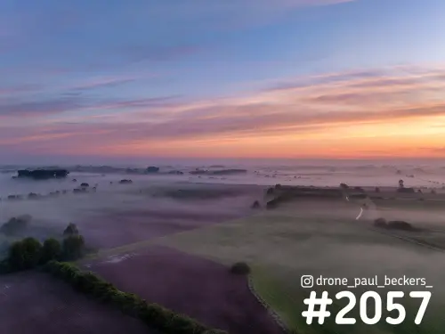 Luchtfoto van de Ooijpolder bij Nijmegen vlak voor zonsopkomst, met mist tussen akkers en bomenrijen onder een roze en oranje lucht