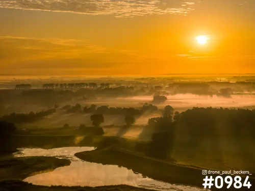 Luchtfoto van de Ooijpolder bij Nijmegen met laaghangende mist, bomenrijen en een kronkelende waterloop onder een oranje zonsopkomst