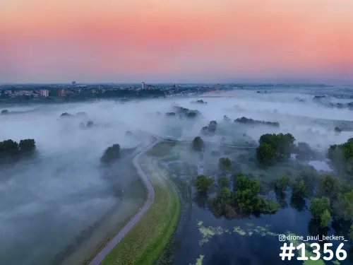 Luchtfoto van de Ooijpolder in de mist met de Waalbrug en Nijmegen in de verte onder een roze ochtendhemel