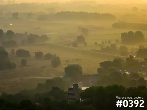 Luchtfoto van de Ooijpolder bij Nijmegen in ochtendmist, met een slingerende weg en bomen in gouden zonlicht