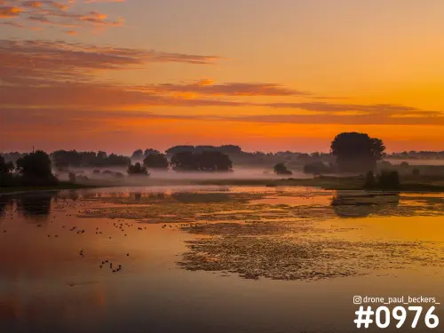 Luchtfoto van de Ooijpolder bij zonsopkomst met oranje lucht, laaghangende mist en watervogels op het spiegelende water