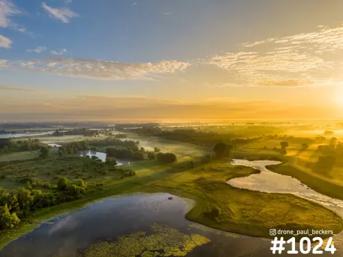 Luchtfoto van de Ooijpolder bij zonsopkomst, met gouden licht over plassen, groene oevers en bomen in de ochtenddamp