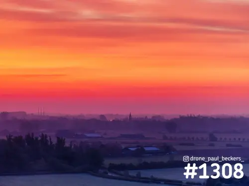 Luchtfoto van de Ooijpolder bij Nijmegen met oranjerode zonsopkomst, lage mist en een kerktorentje aan de horizon