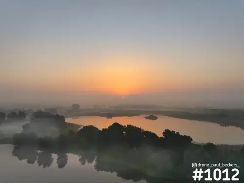 Luchtfoto van de Ooijpolder bij zonsopkomst, met mist boven een plas en oranje licht dat weerkaatst in het water