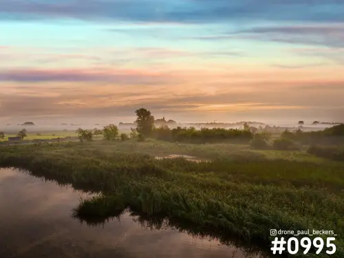 Luchtfoto van de Ooijpolder bij zonsopkomst met rietkragen en stilliggend water, mist boven het land en een roze lucht