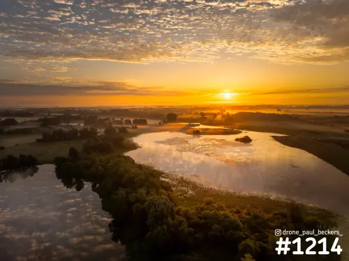 Luchtfoto van de Ooijpolder bij zonsopkomst, met een glinsterende rivierarm en lage mist boven de bomen
