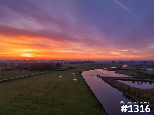 Luchtfoto van de Ooijpolder bij zonsopkomst, met een kronkelende waterloop, natte weilanden en een oranje en paarse lucht