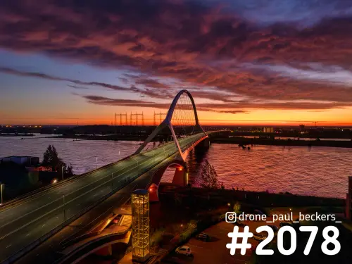 Luchtfoto van de Oversteek in Nijmegen bij zonsondergang, met een oranjerode wolkenlucht boven de Waal bij Lent