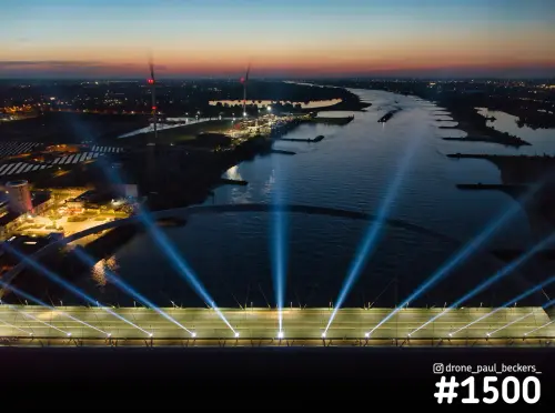 Luchtfoto van De Oversteek in Nijmegen in de schemering, met lichtbundels vanaf het brugdek en de Waal op de achtergrond