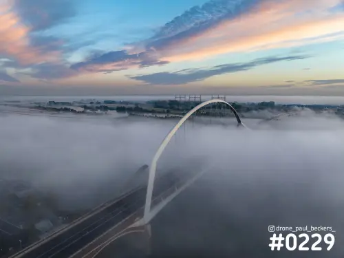 Luchtfoto van De Oversteek in Nijmegen met de witte boog boven de mist op de Waal, onder een roze en blauwe lucht
