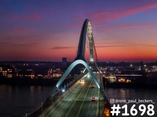 Luchtfoto van de Oversteek in Nijmegen in de schemering, met verlichte boog en auto's op het brugdek boven de Waal