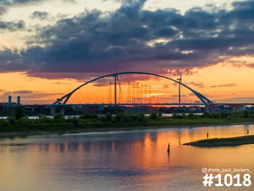 Luchtfoto van De Oversteek over de Waal bij Nijmegen na zonsondergang, met oranje wolkenlucht die weerspiegelt in het water