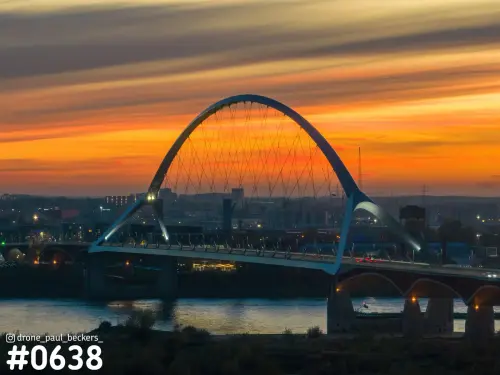 Luchtfoto van de Oversteek over de Waal in Nijmegen bij zonsondergang, met oranje avondrood achter de boogbrug