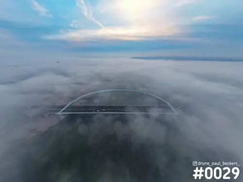 Luchtfoto van brug De Oversteek in Nijmegen, met de witte boogbrug boven een dik mistdek op de Waal