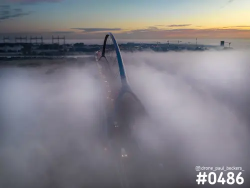 Luchtfoto van de Oversteek in Nijmegen met de boog van de brug boven dikke mist op de Waal bij zonsopkomst