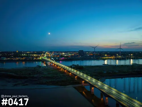 Luchtfoto van de verlichte brug De Oversteek over de Waal in Nijmegen in de blauwe schemering, met maan en windmolens