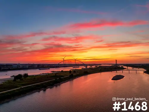 Luchtfoto van De Oversteek over de Waal bij Nijmegen onder een rood-oranje avondlucht, met de nevengeul op de voorgrond