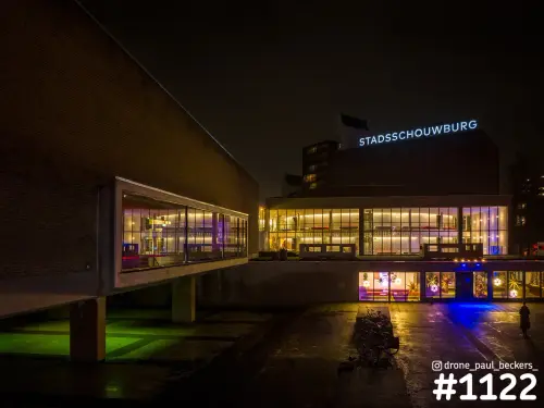 Stadsschouwburg in Nijmegen in de avond met verlichte letters, glazen foyer en nat plein met blauw en groen licht