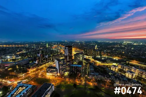 Luchtfoto van het Stationsgebied in Nijmegen in de avondschemering, met verlichte hoogbouw en een roze-oranje horizon
