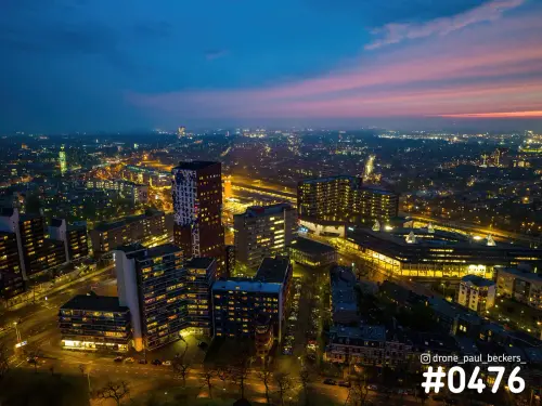 Luchtfoto van het stationsgebied in Nijmegen in het blauwe uur, met verlichte hoogbouw en roze avondlucht boven de stad