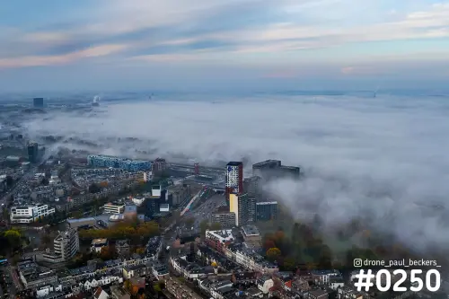 Luchtfoto van mist boven het Stationsgebied in Nijmegen, met hoogbouw bij Nimbus en herfstbomen in het Kronenburgerpark