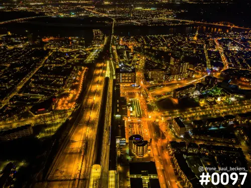 Luchtfoto van het stationsgebied in Nijmegen bij nacht, met verlichte sporen en perrons en De Oversteek aan de horizon