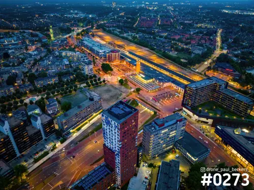 Luchtfoto van toren Nimbus en het stationsgebied in Nijmegen in het blauwe uur, met verlichte perrons en kruispunt