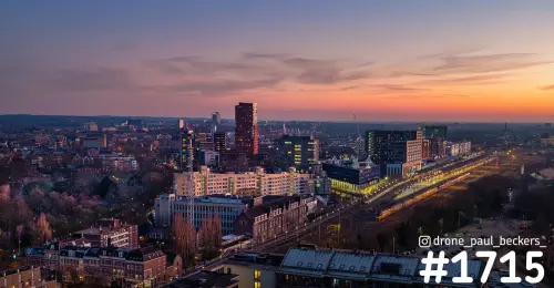 Luchtfoto van het stationsgebied in Nijmegen in de schemering, met een trein langs het spoor en een oranje lucht