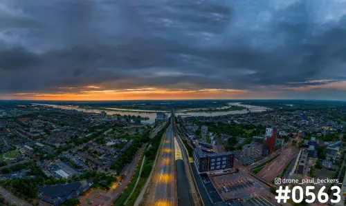Luchtfoto van het Stationsgebied in Nijmegen bij schemering, met spoorbaan en een oranje horizon onder donkere wolken