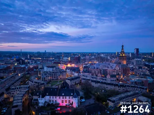 Luchtfoto van het centrum van Nijmegen in de schemering met de verlichte Stevenskerk en een wolkenlucht boven de daken