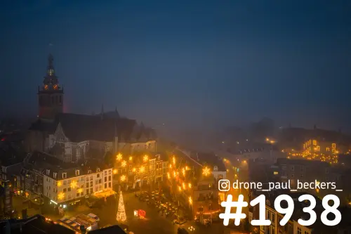Luchtfoto van de Stevenskerk en de Grote Markt in Nijmegen in de avondmist, met kerstverlichting en een verlichte kerstboom