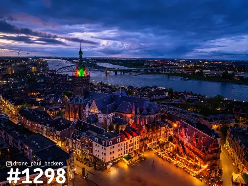 Luchtfoto van de Stevenskerk en de Grote Markt in Nijmegen in het blauwe uur, met de Waal en verlichte terrassen