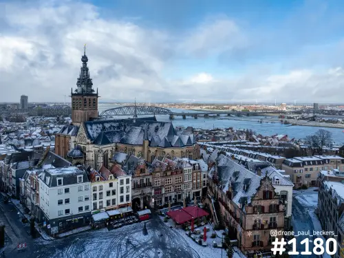 Luchtfoto van de Stevenskerk en de Grote Markt in Nijmegen onder een laagje sneeuw, met de Waal en de spoorbrug op de achtergrond