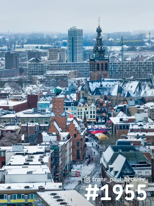 Luchtfoto van de besneeuwde daken van het centrum van Nijmegen met de Stevenskerk en kraampjes op de Grote Markt