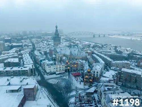 Luchtfoto van de Stevenskerk en de Grote Markt in Nijmegen onder de sneeuw, met mist boven de Waal en de spoorbrug