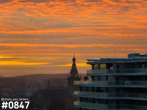 De toren van de Stevenskerk in Nijmegen tegen een oranje avondlucht, naast het appartementencomplex aan de Handelskade