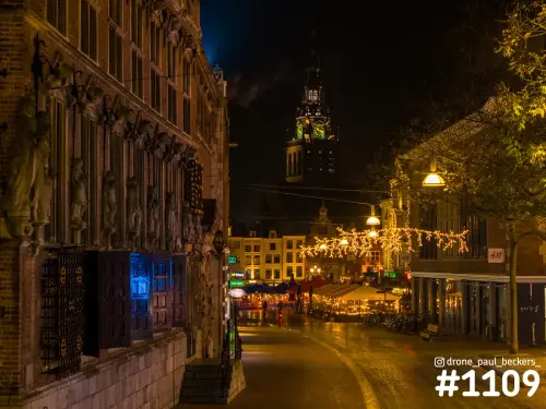 Verlichte toren van de Stevenskerk in Nijmegen 's avonds, boven een straat met lichtslingers en terrastenten