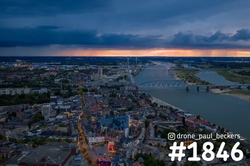Luchtfoto van het centrum van Nijmegen met de Stevenskerk en de Waal in de avondschemering onder een donkere onweerslucht