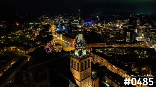 Luchtfoto van de verlichte Stevenskerk in Nijmegen 's avonds, met de toren boven de stad en lichtgevende straten