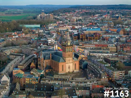 Luchtfoto van de Stevenskerk in het centrum van Nijmegen in avondlicht, met verlichte gevels en daken eromheen